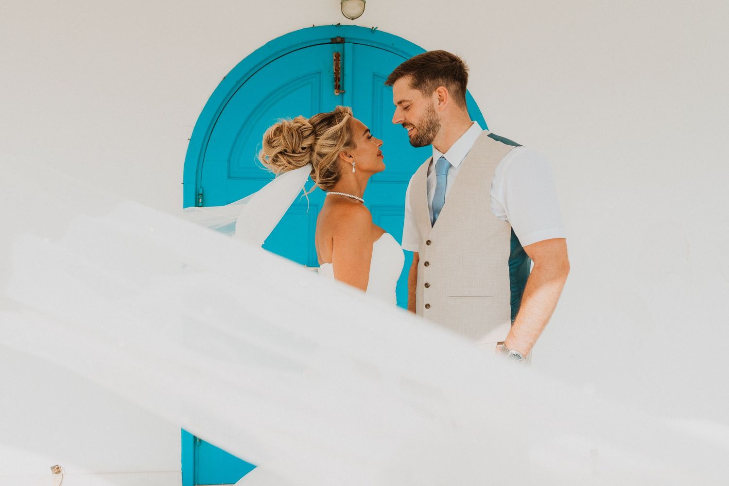 Bride and groom share a romantic moment in front of a turquoise door at a destination wedding.