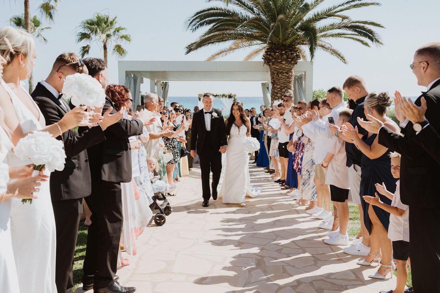 Wedding party celebrating outdoors with palm trees and ocean views at a beachside ceremony.