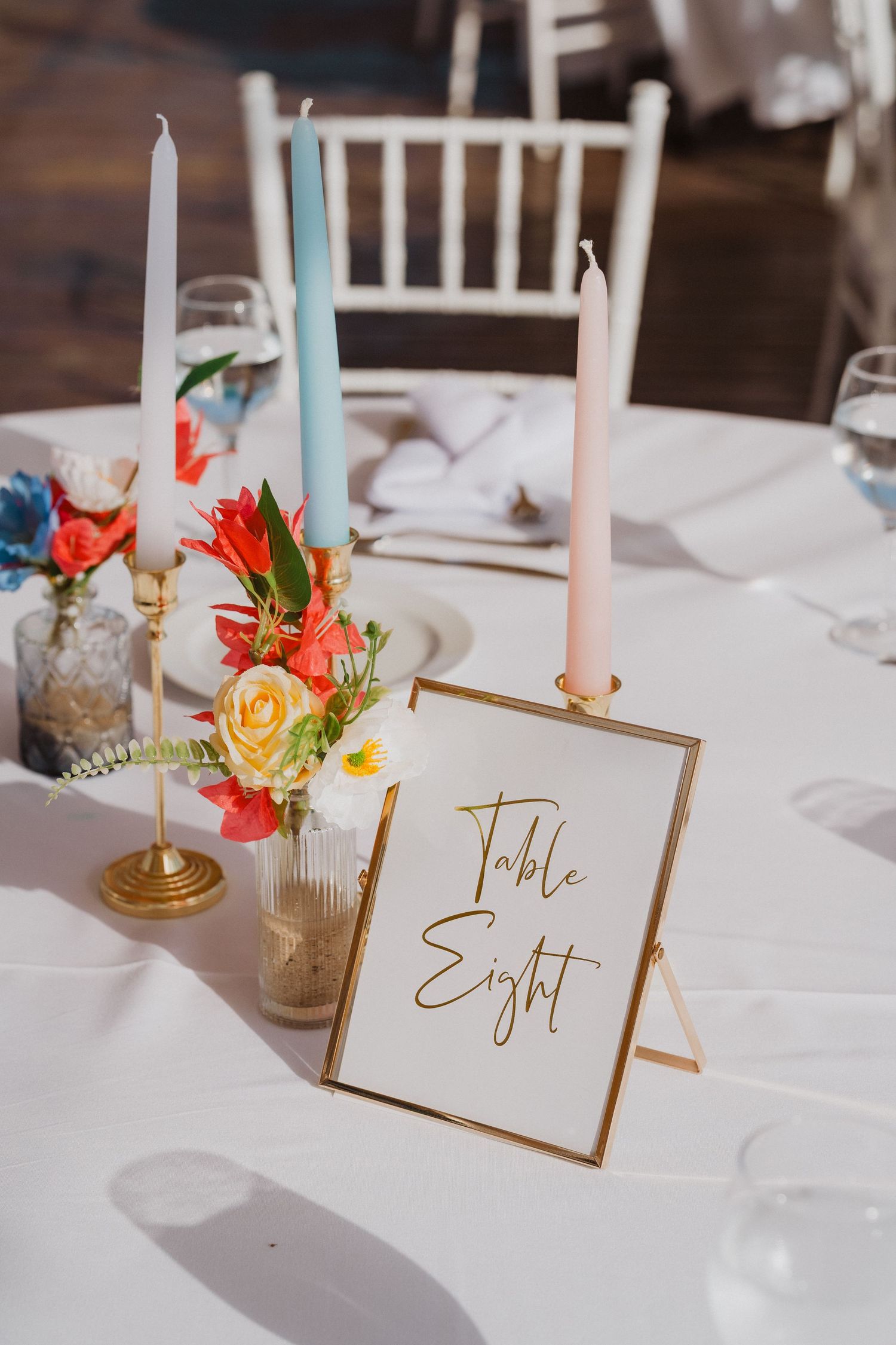 Wedding reception table settings with gold framed table numbers and delicate floral centerpieces with taper candles.