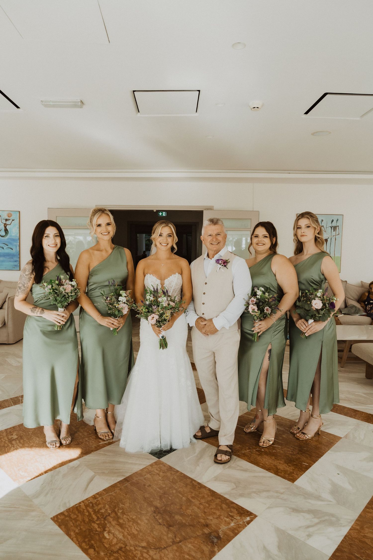 Wedding party lined up indoors with bridesmaids in sage green dresses.