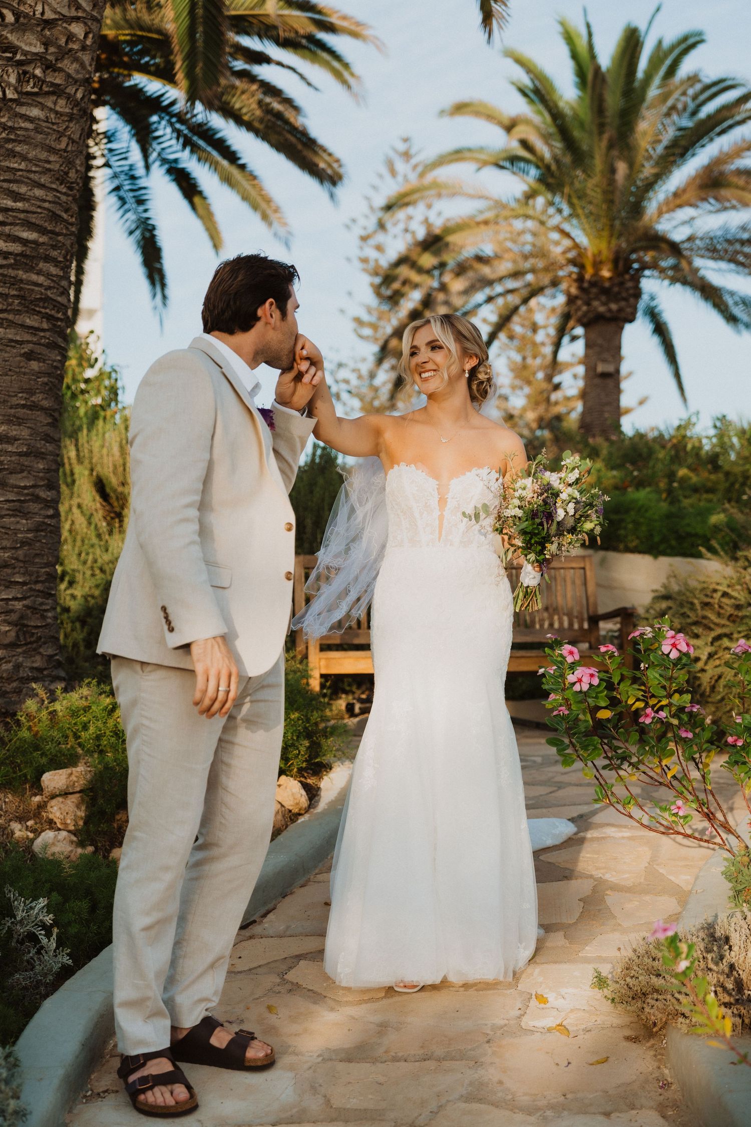 Romantic wedding moment captured in a garden with palm trees and stone pathway.