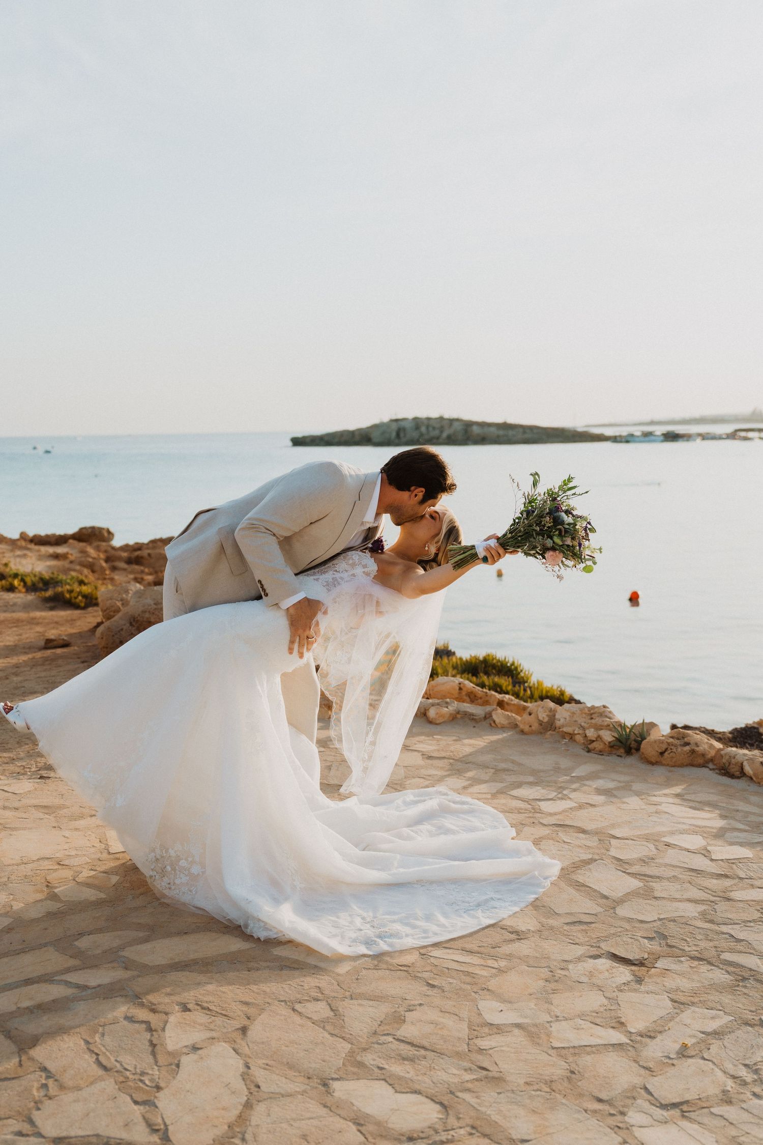 Dramatic dip pose wedding photos on stone pathway overlooking Mediterranean waters.