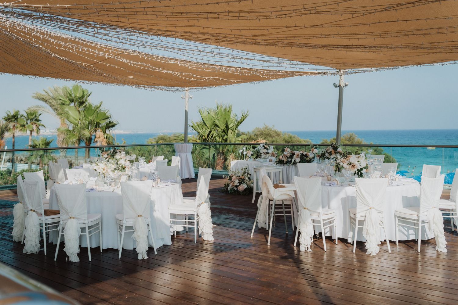 Seaside wedding reception venue with white tables and chairs under tan shade sails.