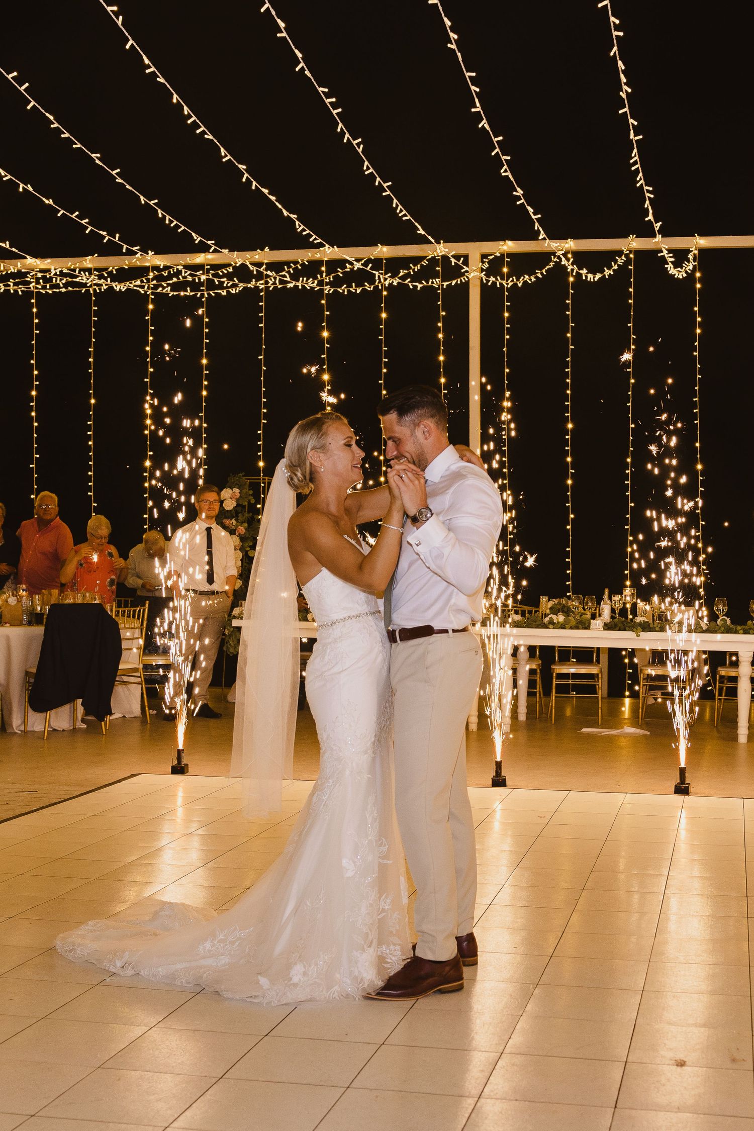 A couple embraces during their wedding dance beneath a canopy of twinkling fairy lights.