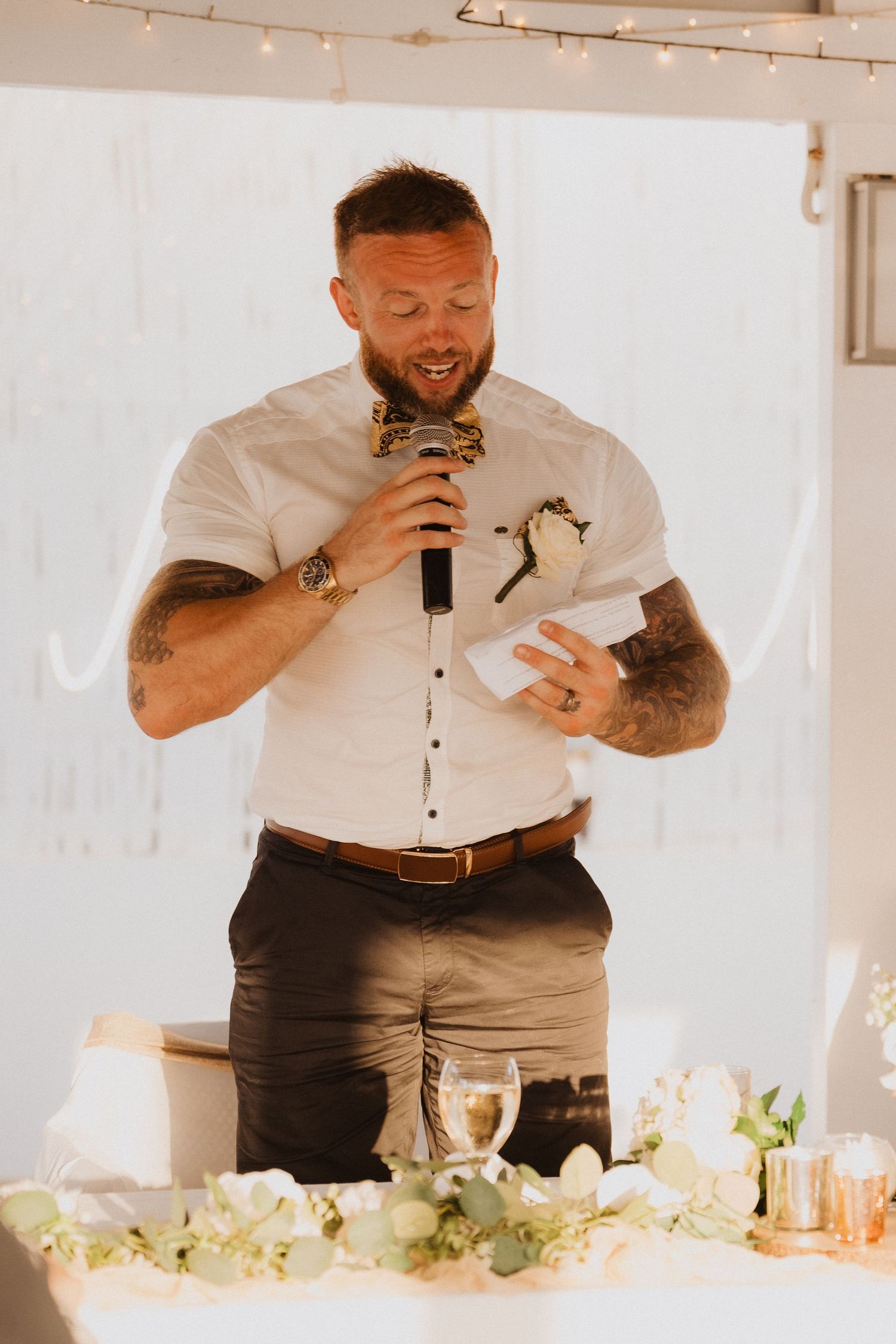 Wedding speech moment at decorated reception table with floral centerpieces and ambient lighting.