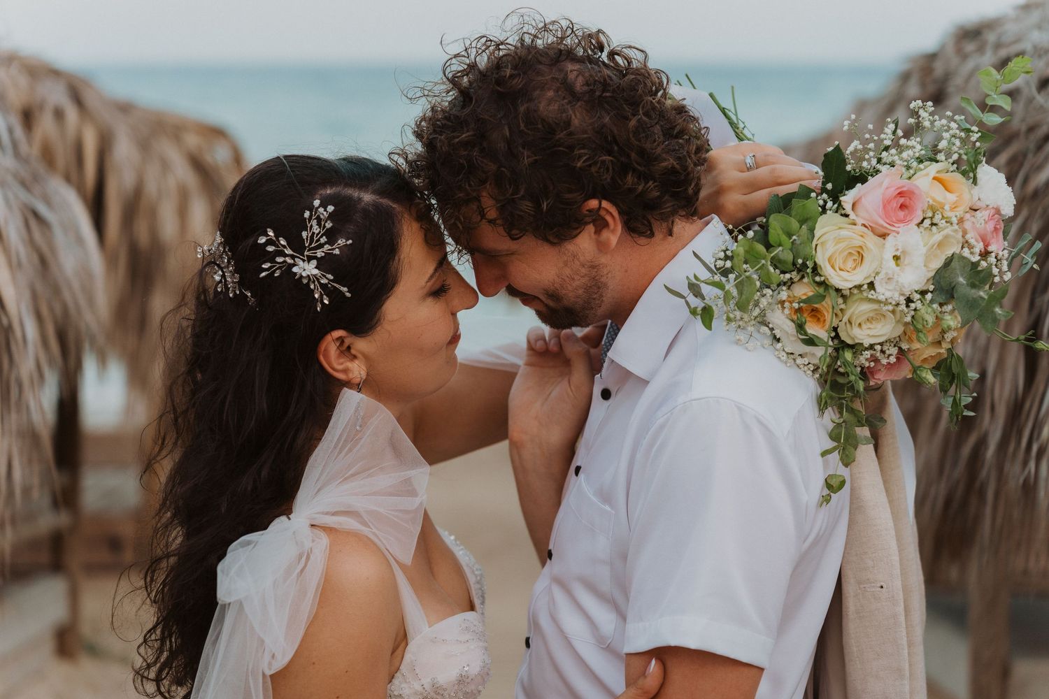 A romantic beach wedding moment with a bride in white dress and groom in casual attire sharing an intimate moment.