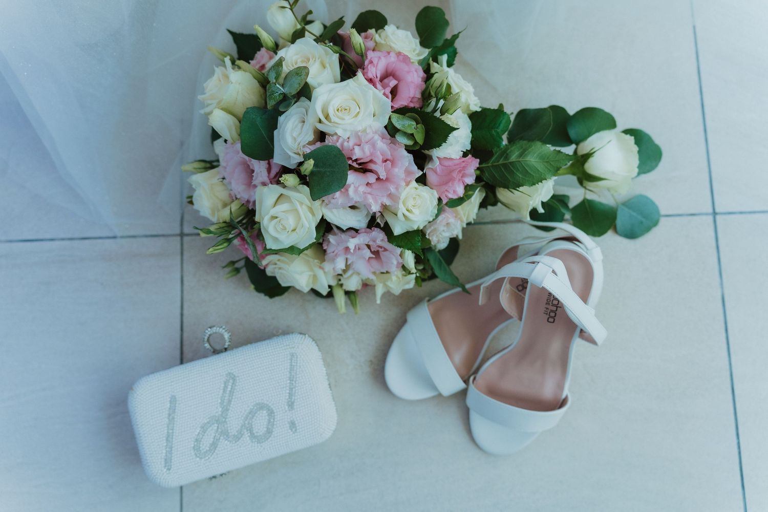 An elegant bridal bouquet with white and pink flowers alongside wedding shoes and a 'I do' sign.