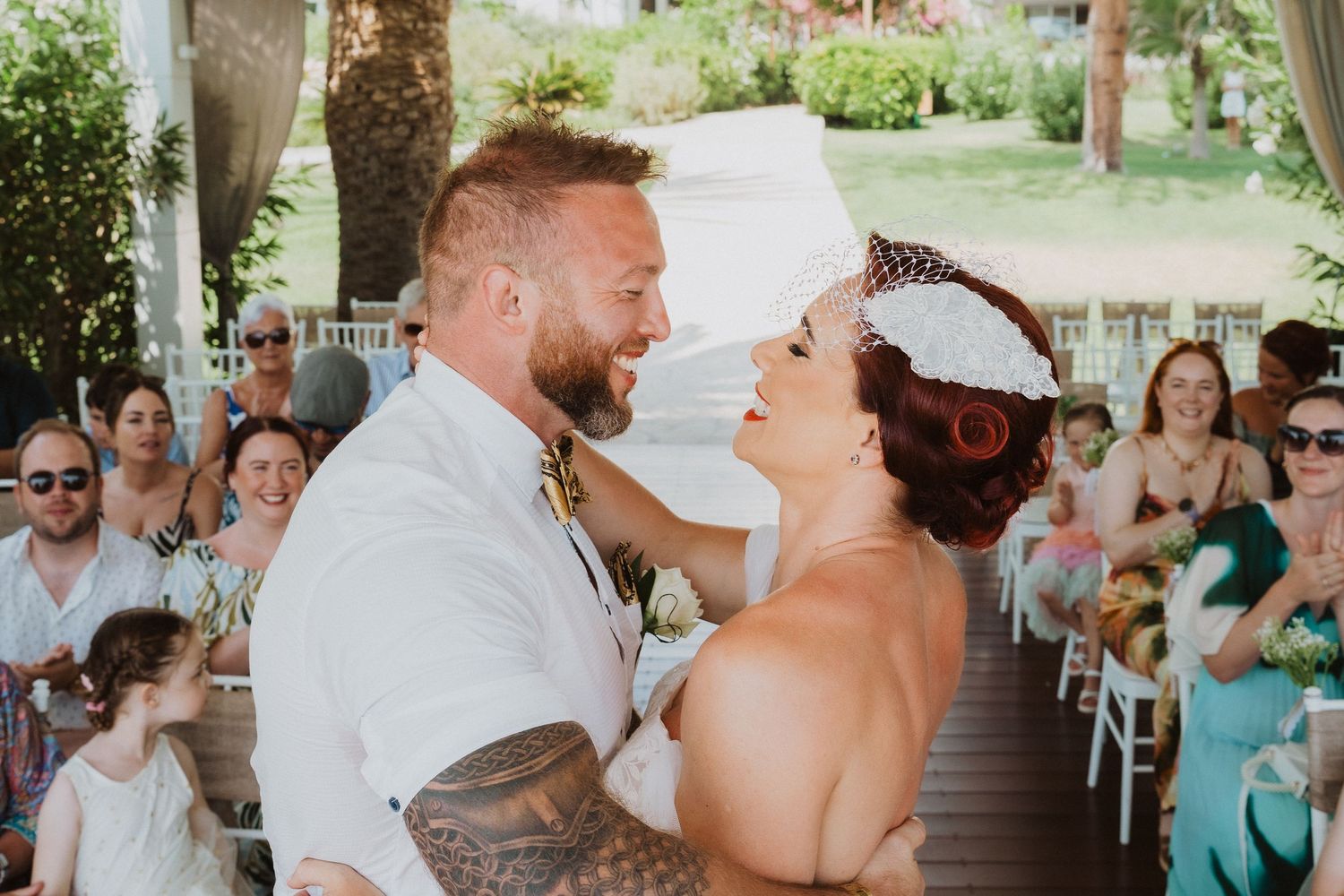 An intimate wedding moment captured on a covered porch with guests watching in the background.