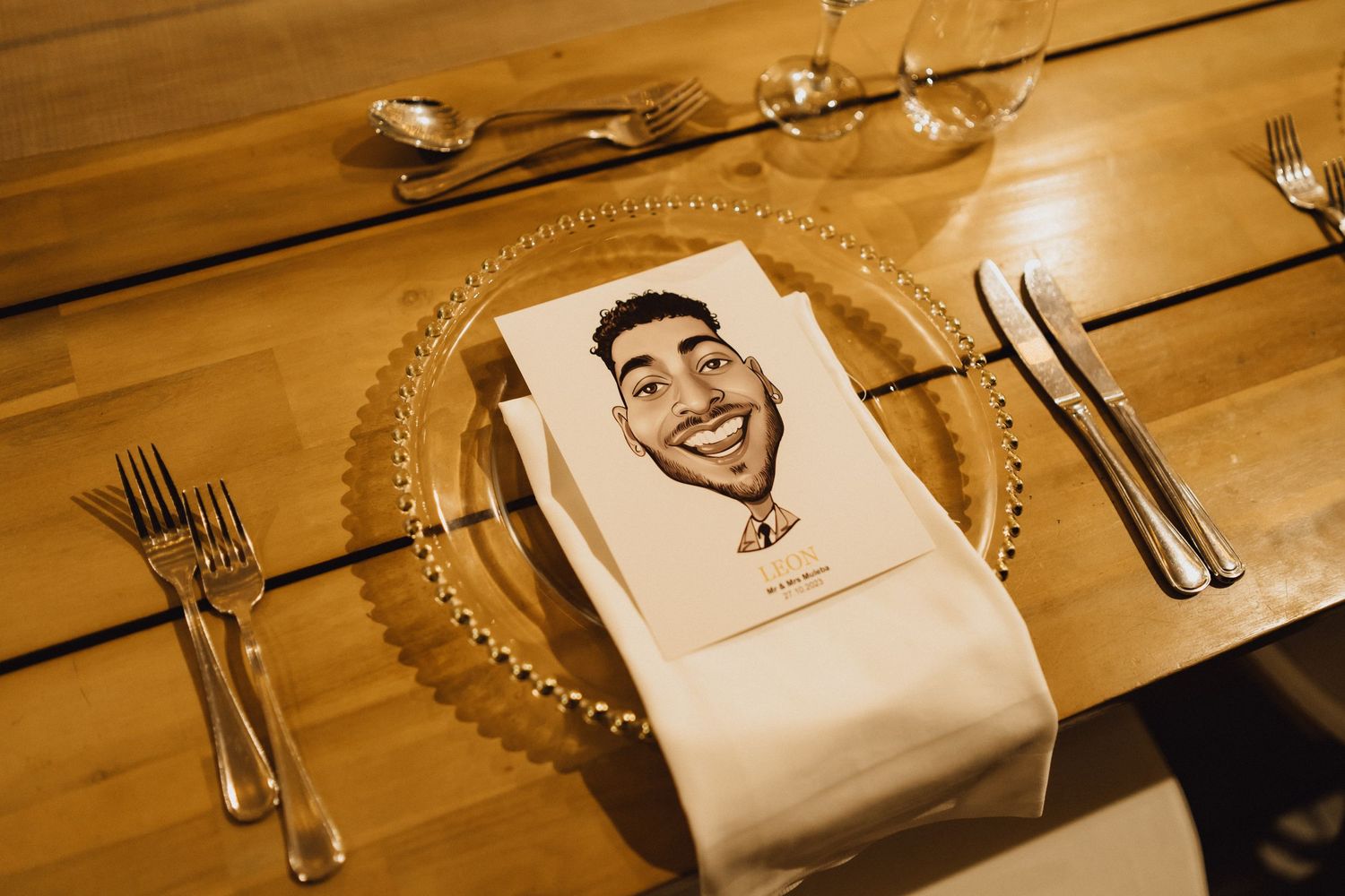 A decorative place setting at a wedding reception with a custom napkin illustration on a wooden table.