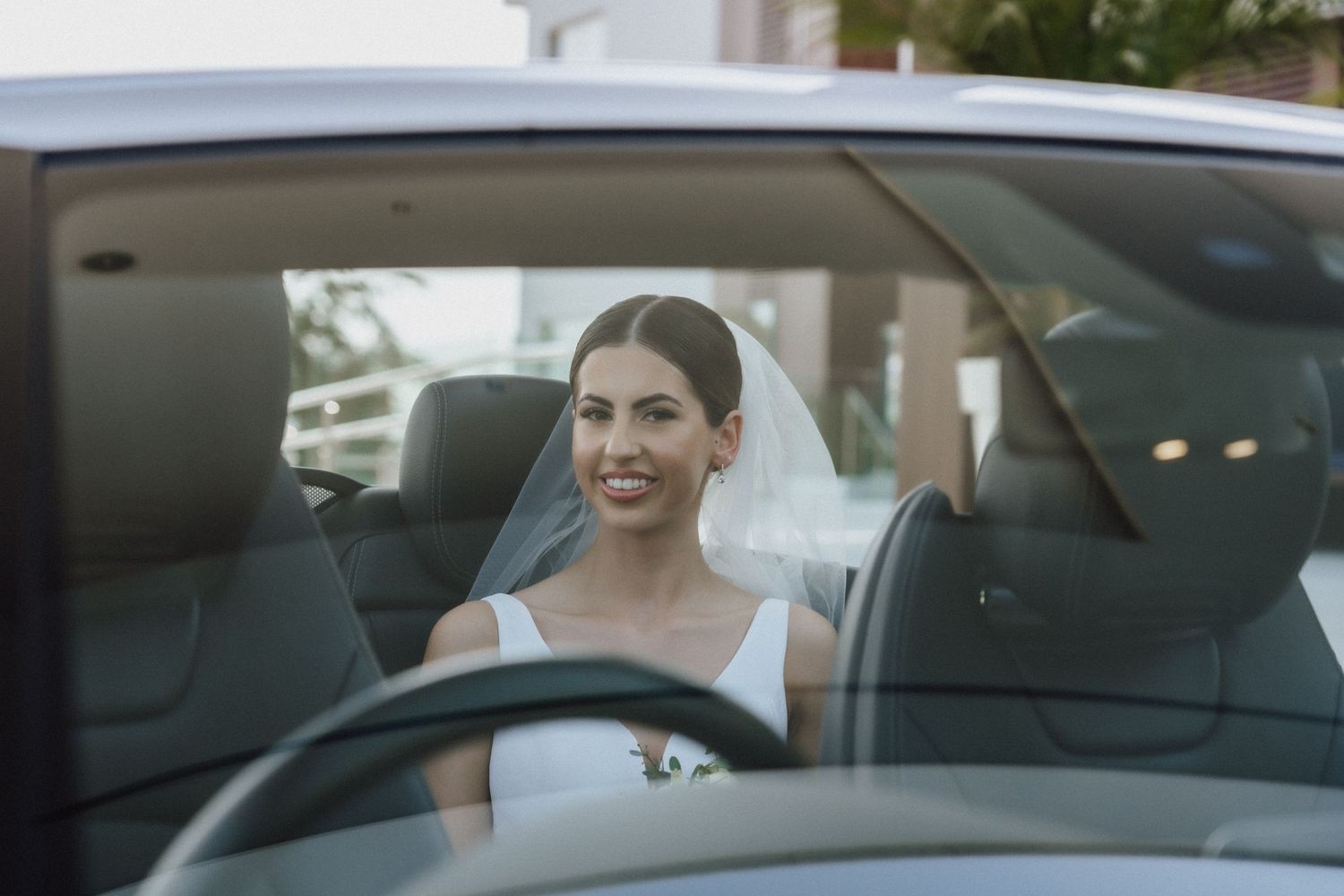 A person sits behind the wheel of a sleek white car on a sunny day.