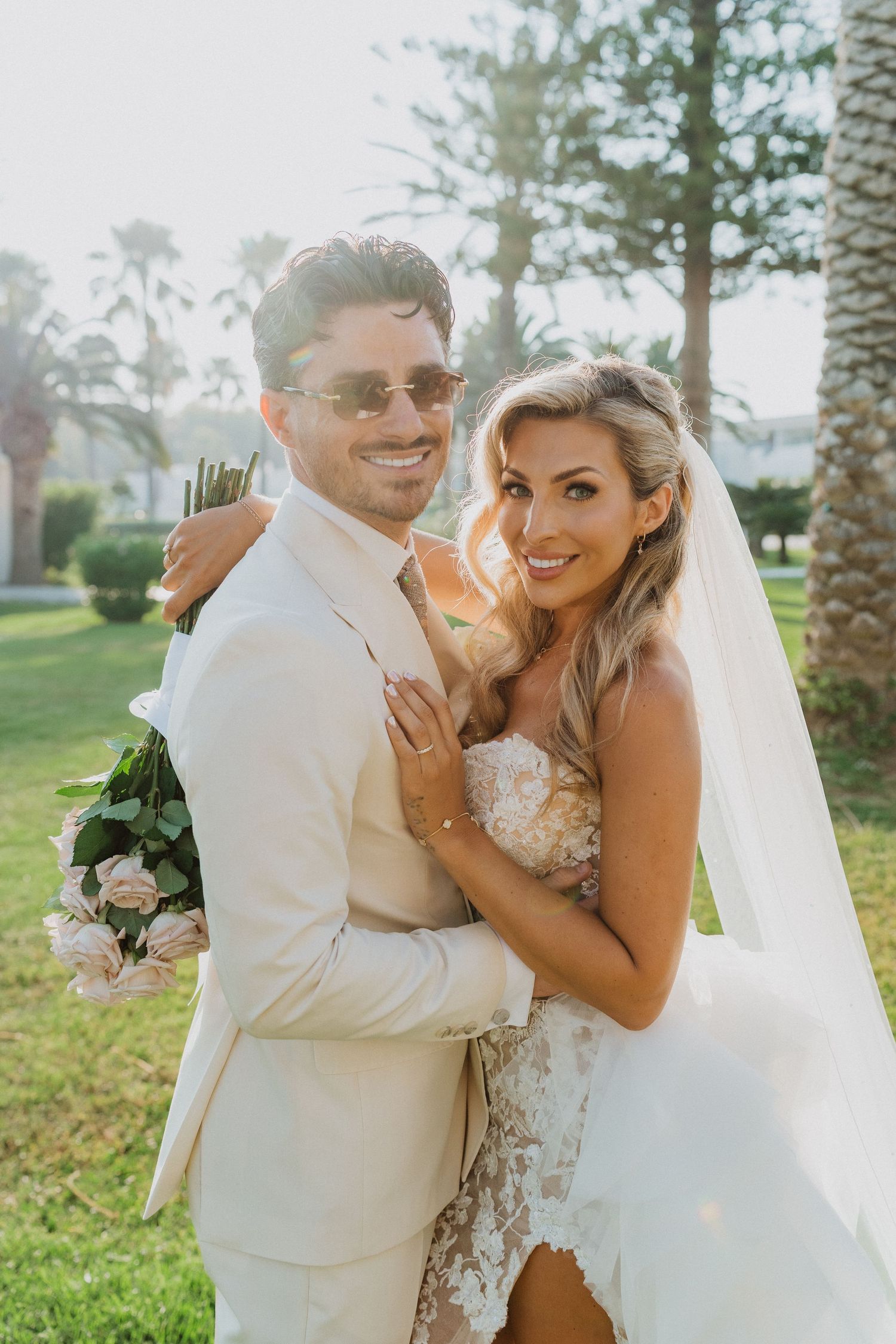 A joyful wedding couple embraces and laughs together outdoors among palm trees during their tropical celebration.