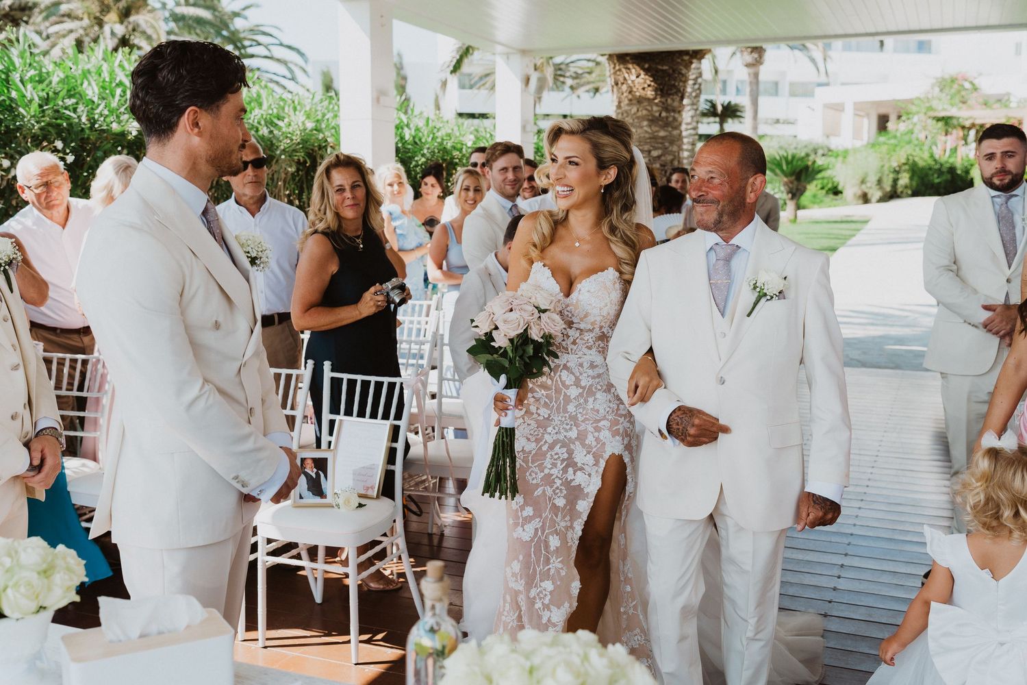 A group of wedding guests dressed in white gather under an elegant outdoor pavilion during a celebration.
