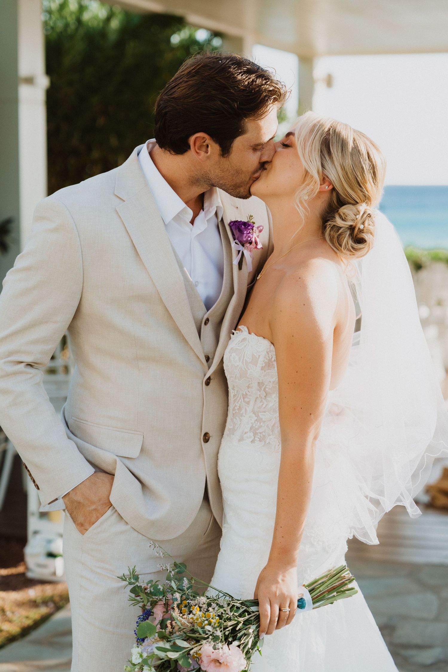 An intimate wedding portrait showing a romantic kiss against a coastal backdrop.
