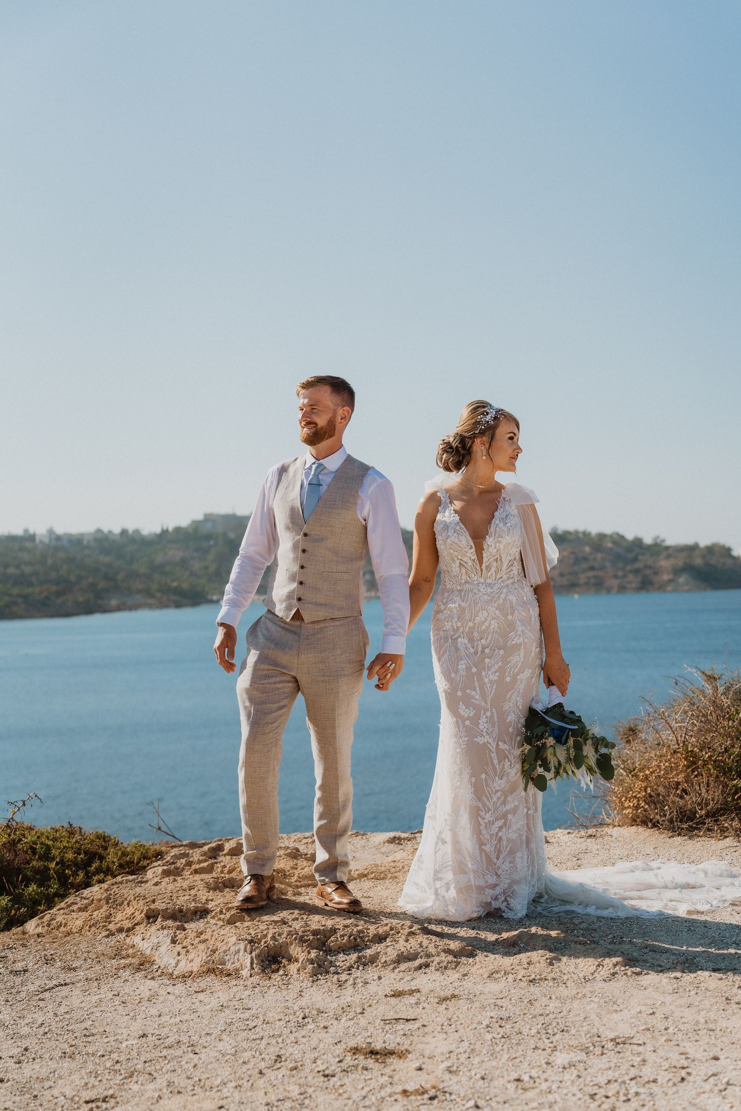 Bride and groom walk along coastal cliff with ocean views.