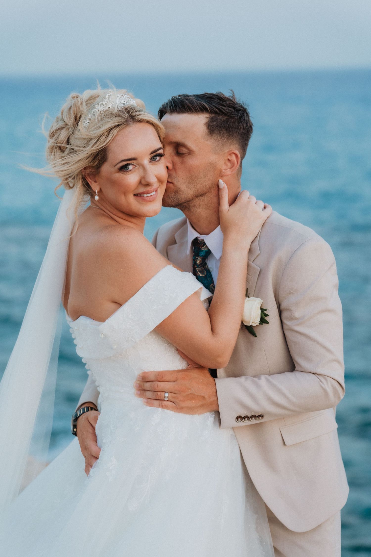 Newlyweds share an intimate moment against a blue ocean backdrop at their beach wedding.