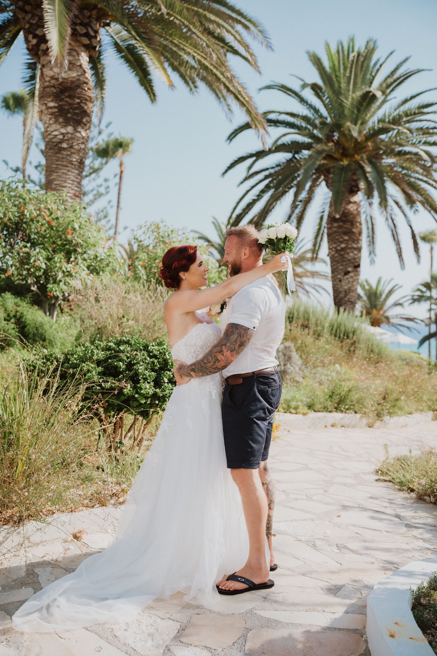 A romantic embrace between newlyweds on a stone path with tropical palm trees in the background.