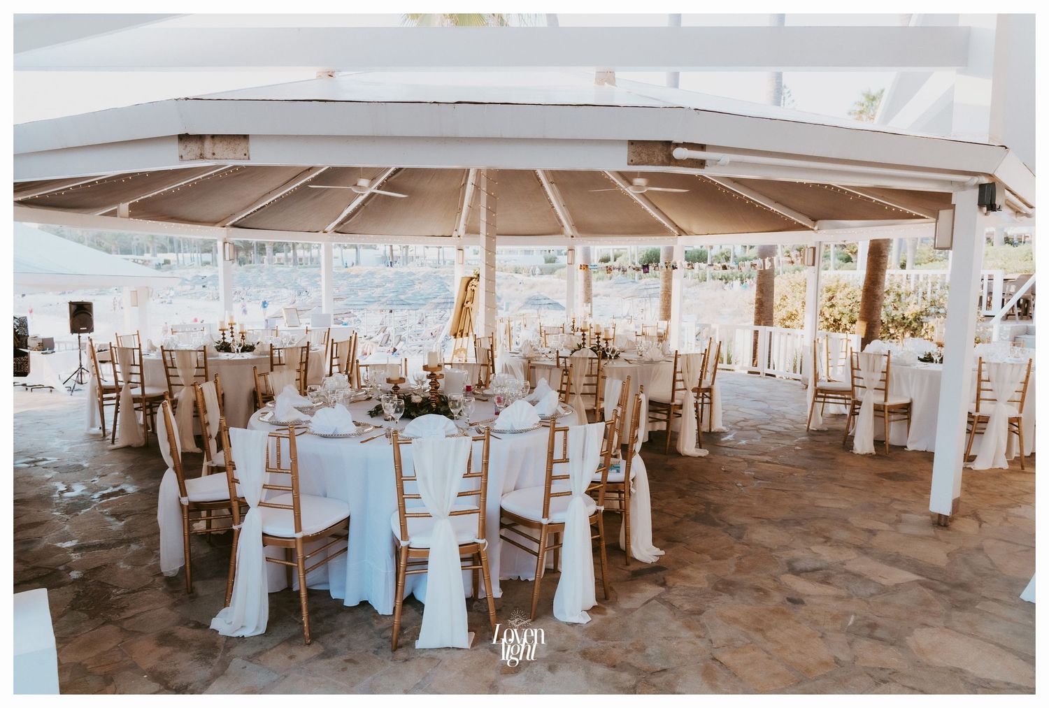 White tent reception setup with elegant table settings and draped chair covers.