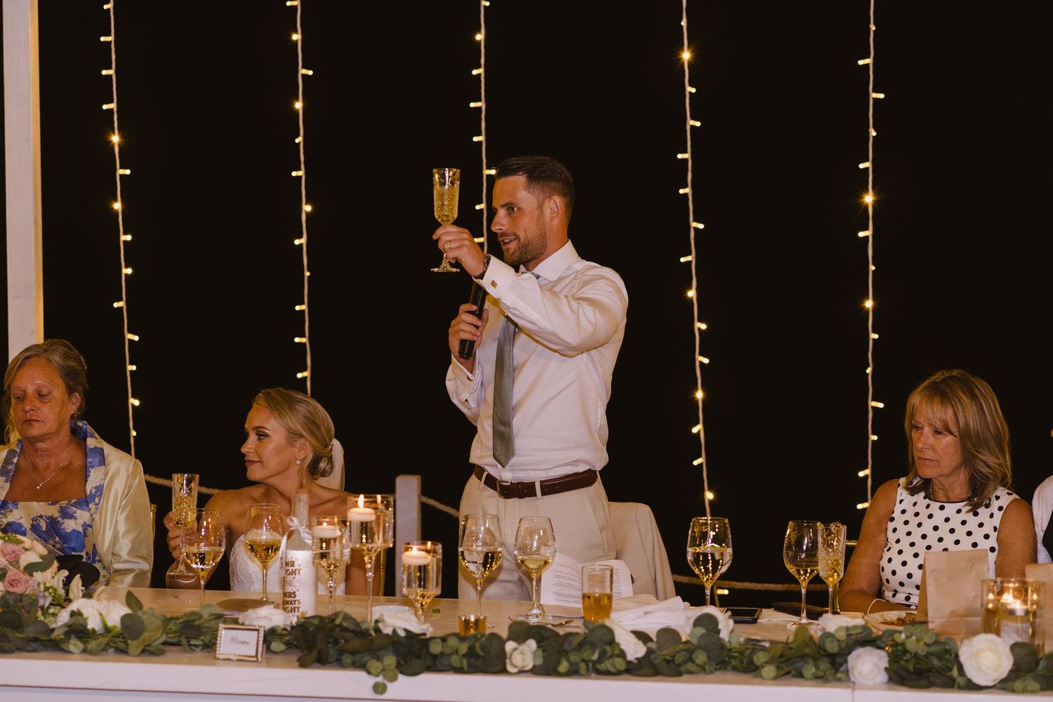 Toast being given at wedding reception with string lights creating romantic backdrop.