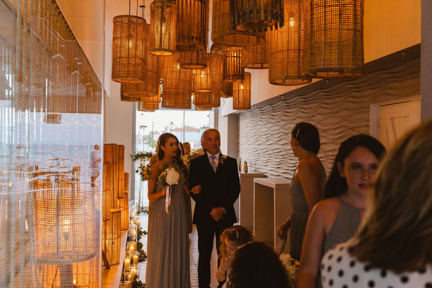 Indoor wedding ceremony with warm lighting and hanging cylindrical lanterns creating an amber atmosphere.
