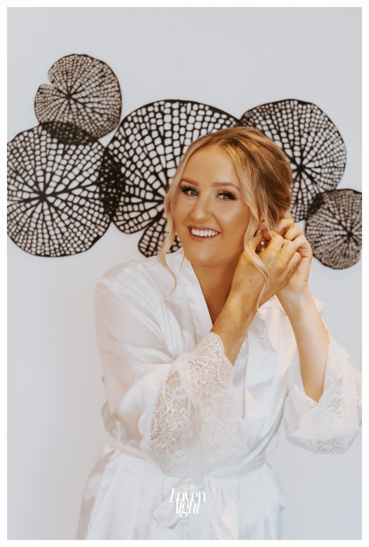 A person in a white lace robe getting ready with decorative circular wall art in the background.