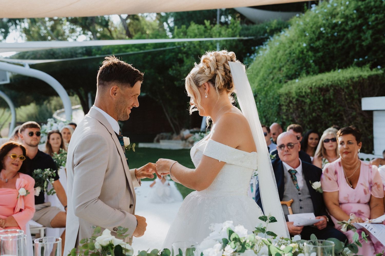 An emotional exchange during a wedding ceremony surrounded by floral decorations and seated guests.