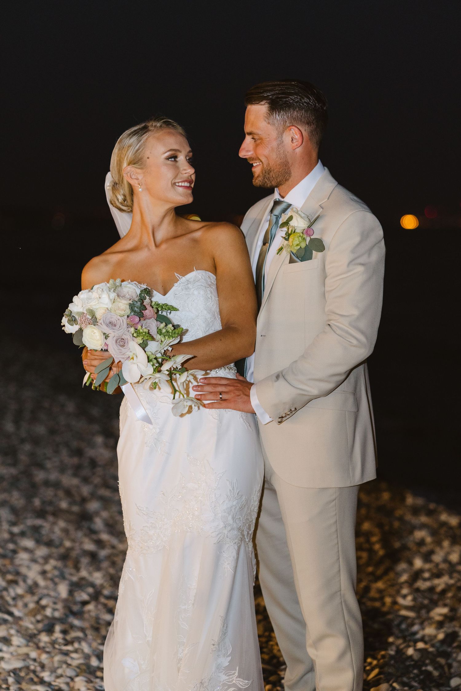 Elegant beachside wedding portrait with couple in light-colored attire sharing a loving moment.
