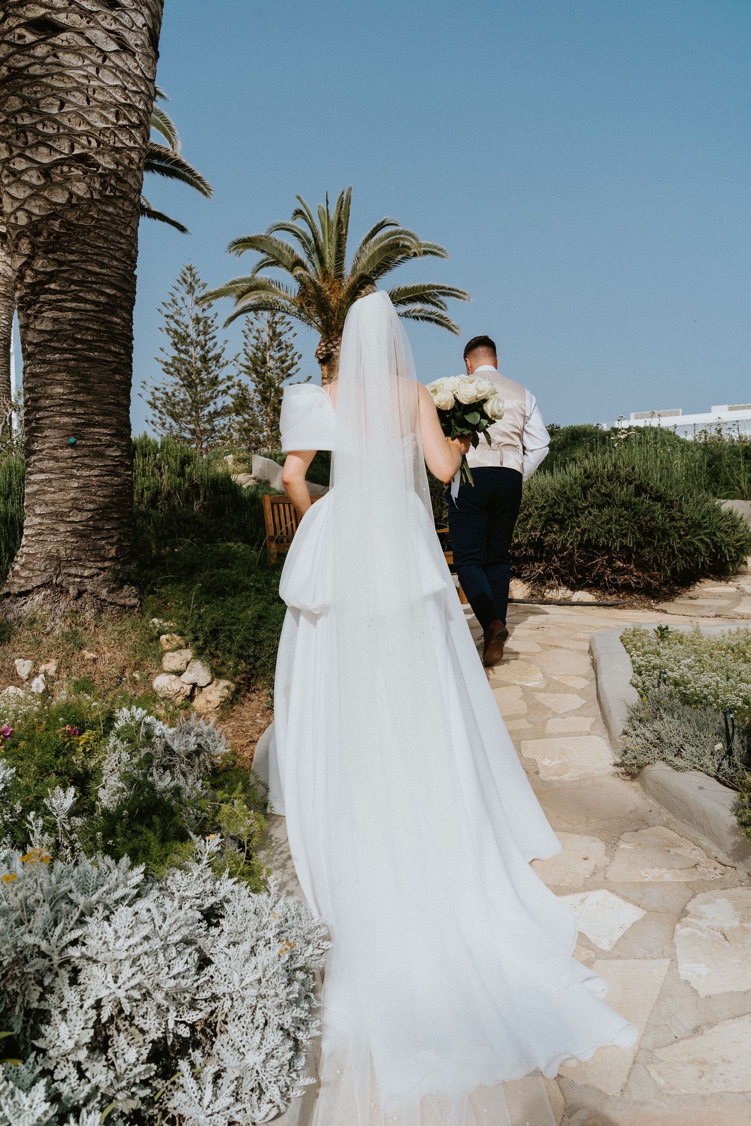 Long flowing wedding dress train on stone path surrounded by tropical landscaping.