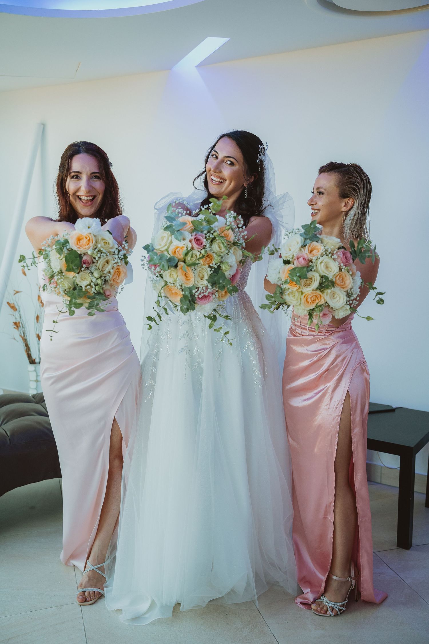 Bride and bridesmaids pose with matching pastel bouquets in elegant wedding attire.