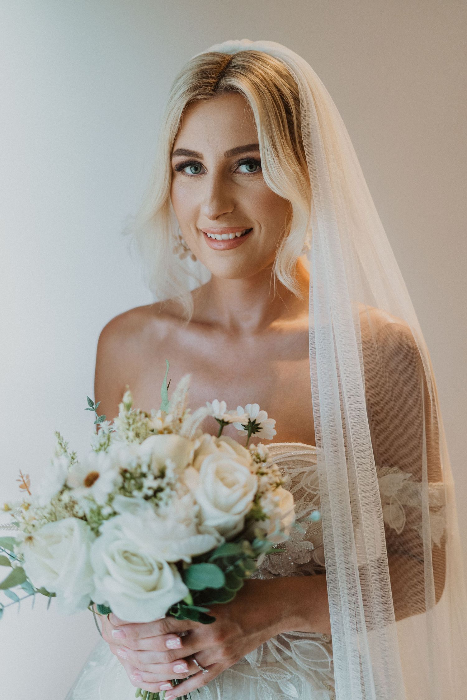 Elegant bridal portrait with white rose bouquet and flowing cathedral veil.
