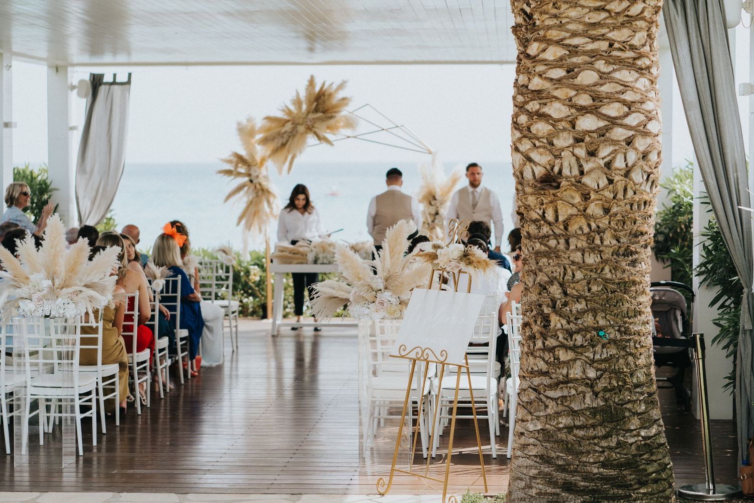 Outdoor wedding reception venue with palm trees and white chairs overlooking the ocean.