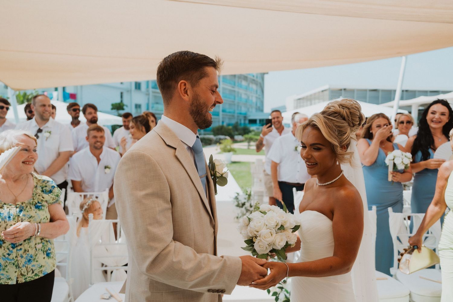Couple exchanging vows at outdoor beach wedding ceremony with guests in background.