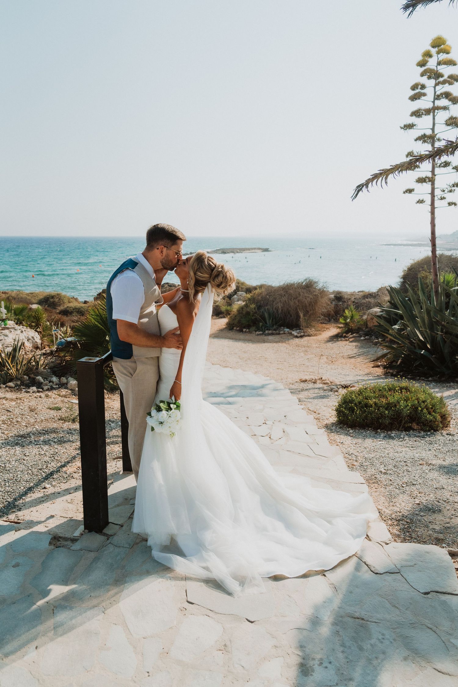 Bride and groom share a romantic kiss by the sea, with a stunning ocean backdrop on their wedding day.