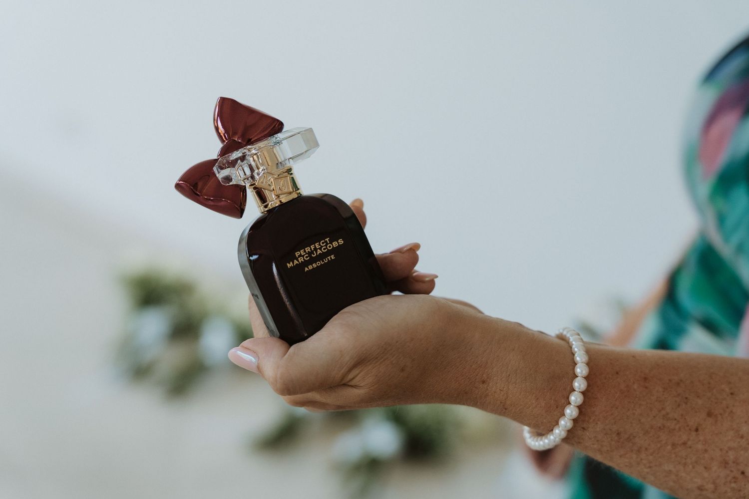Hand holding a perfume bottle against a blurred background with soft teal and white tones.