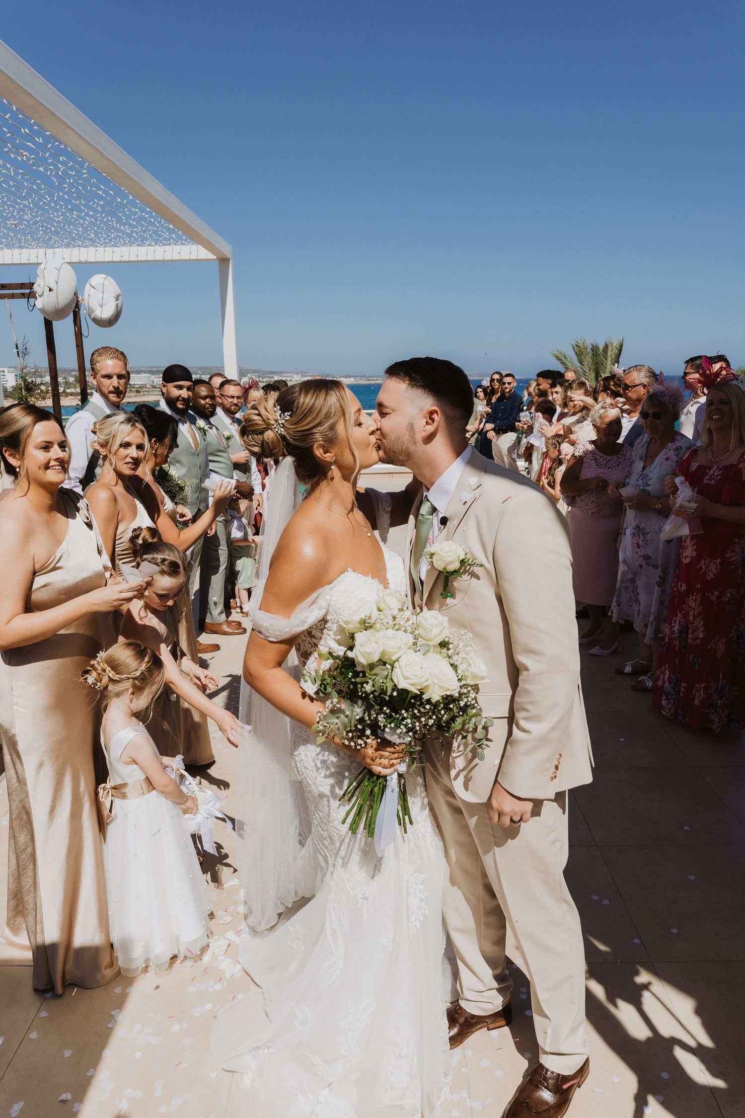 Wedding party celebrates during outdoor ceremony with guests gathered under bright blue sky.