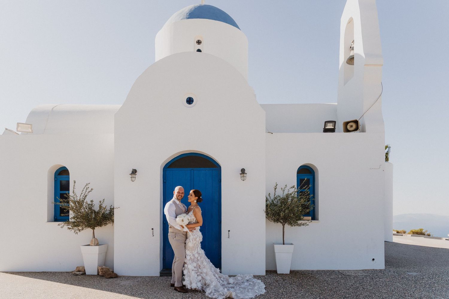 A couple poses in front of white Mediterranean architecture with bright blue doors and arches in Greece.