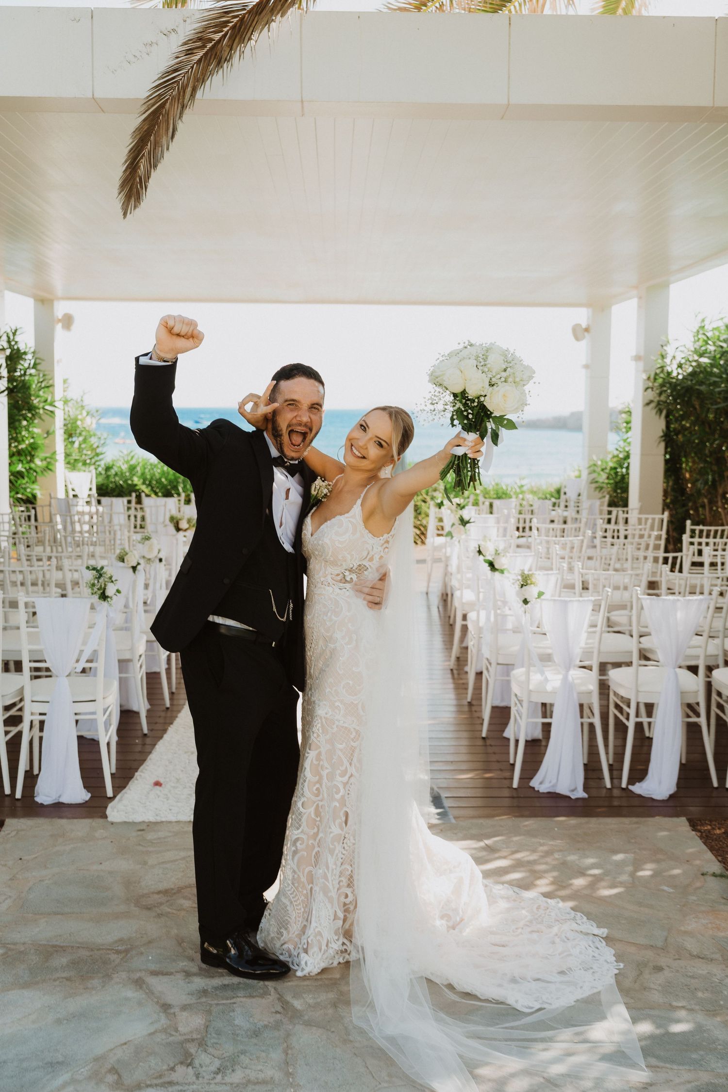 Wedding couple dancing in an elegant white-themed outdoor reception venue with palm trees.