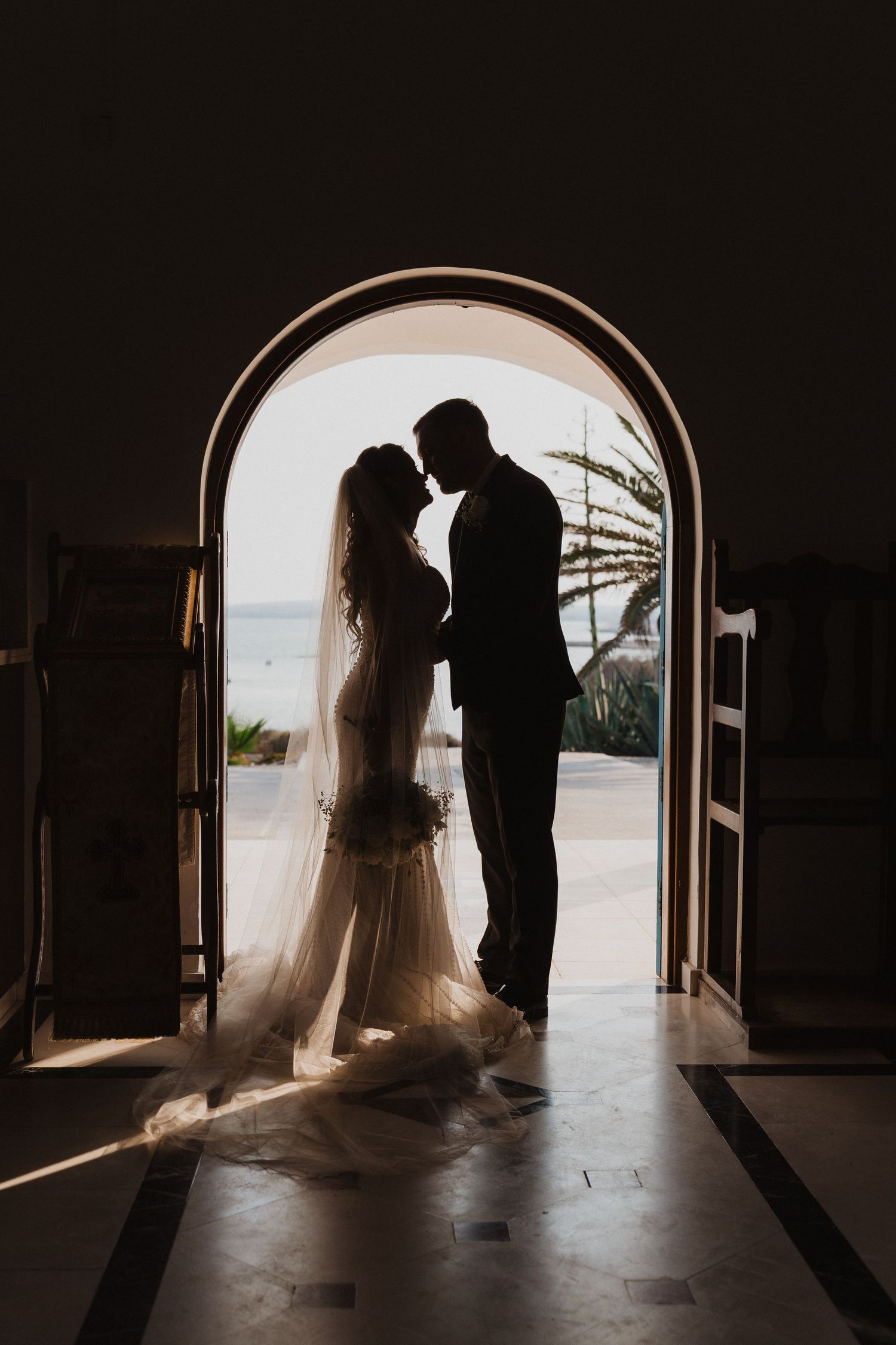 Silhouetted couple shares an intimate moment in an arched doorway overlooking an ocean view.