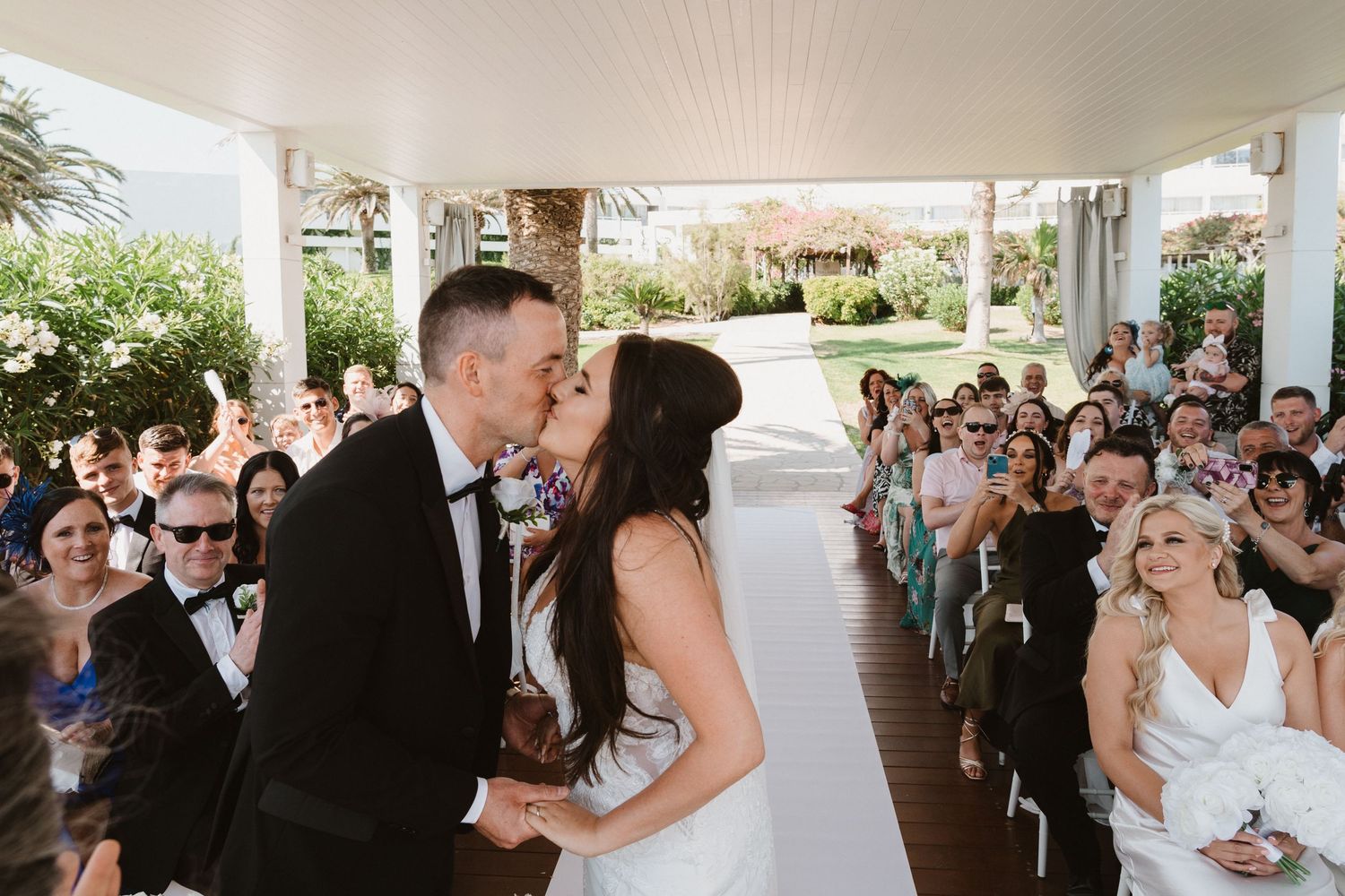 Wedding ceremony guests watch as couple exchanges vows under covered outdoor venue.