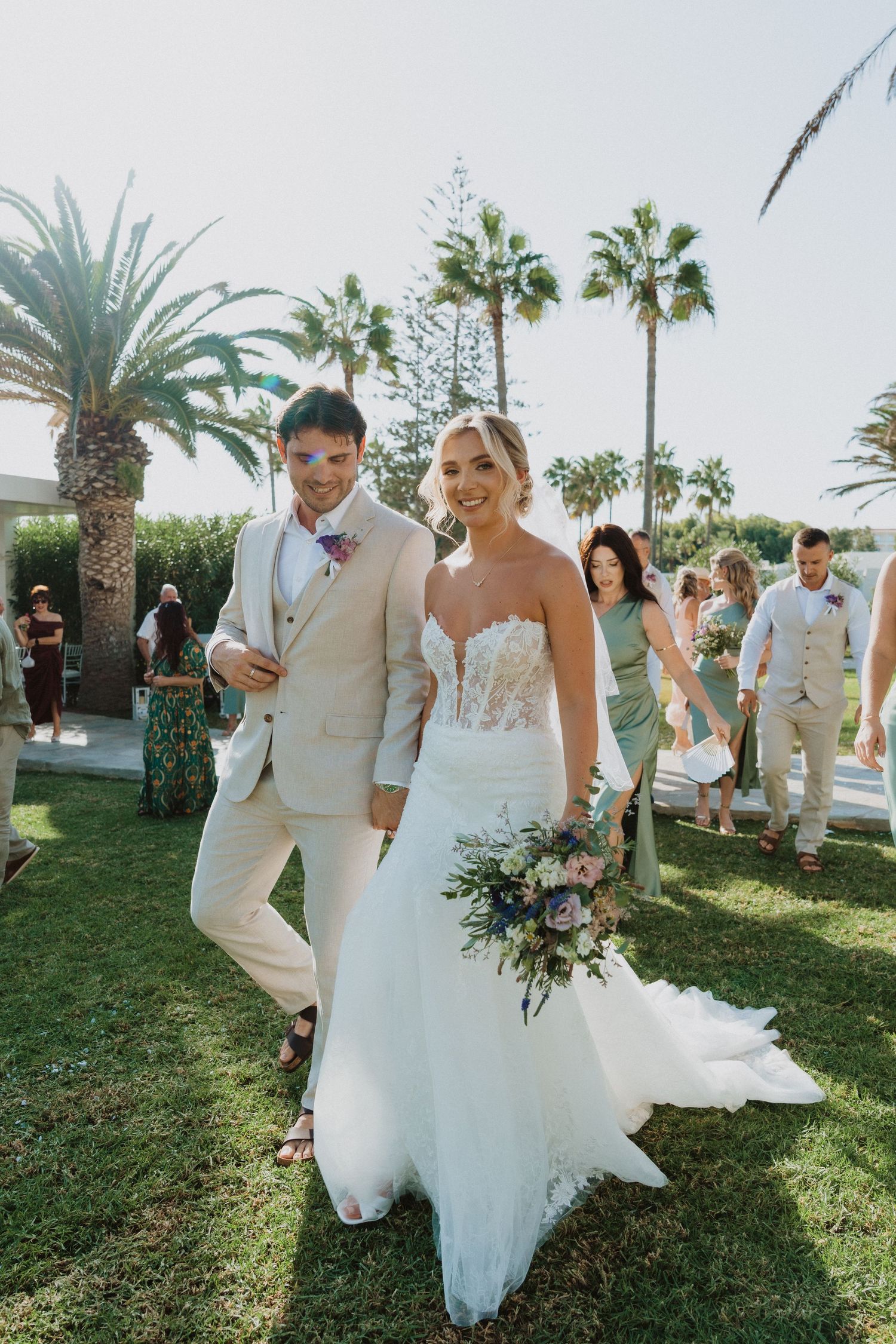 Wedding party walking together on grass with palm trees at a beachside venue.