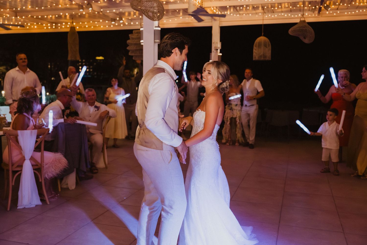 Wedding guests dancing on illuminated dance floor under decorative string lights.
