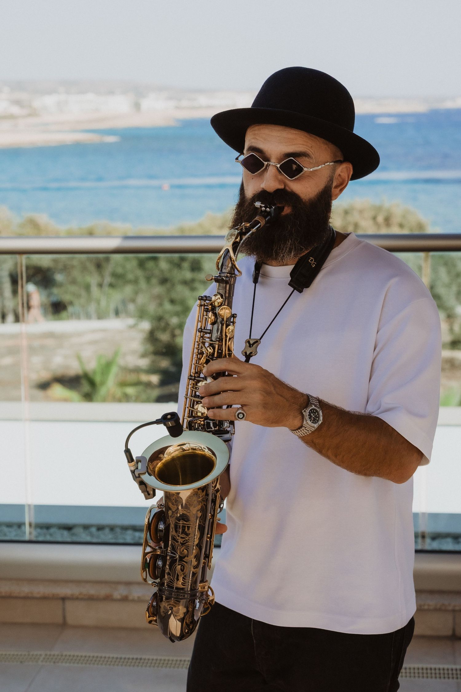 Musician playing saxophone on a balcony overlooking the Mediterranean coastline.