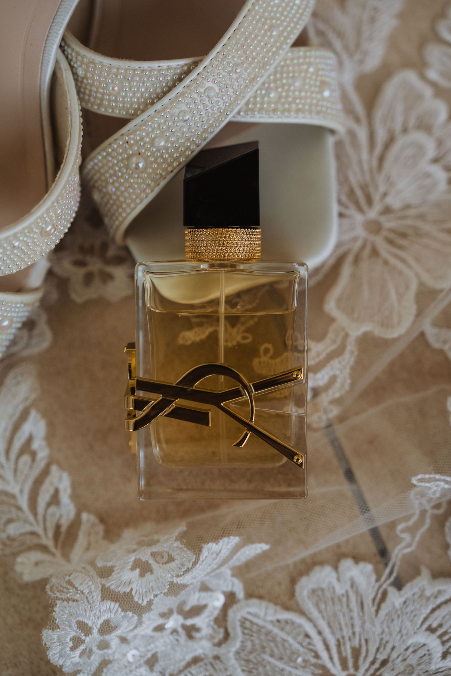 Luxury perfume bottle and sparkly bridal shoes arranged with lace details.