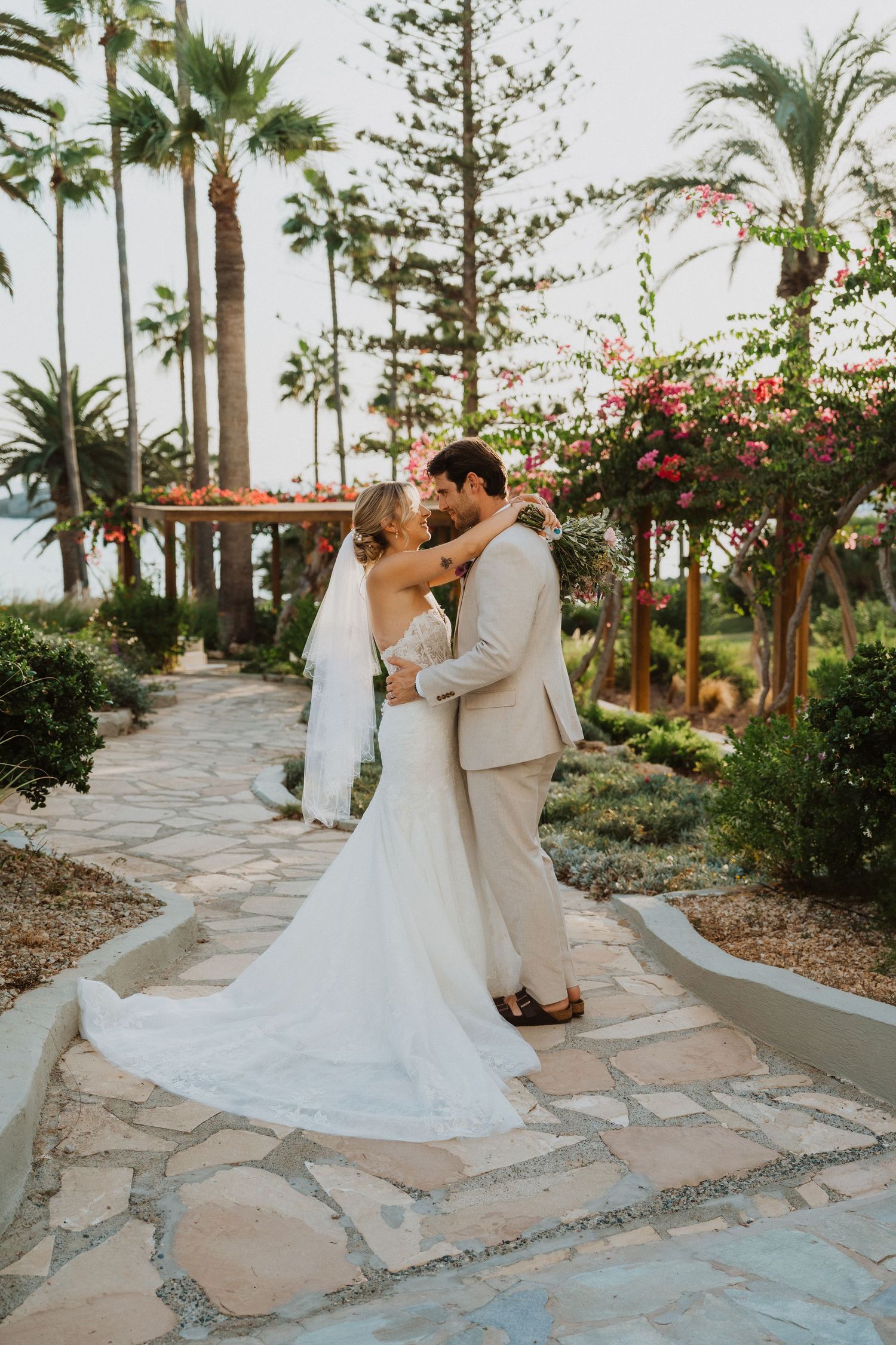 Bride and groom share intimate moments on a stone path surrounded by palm trees.