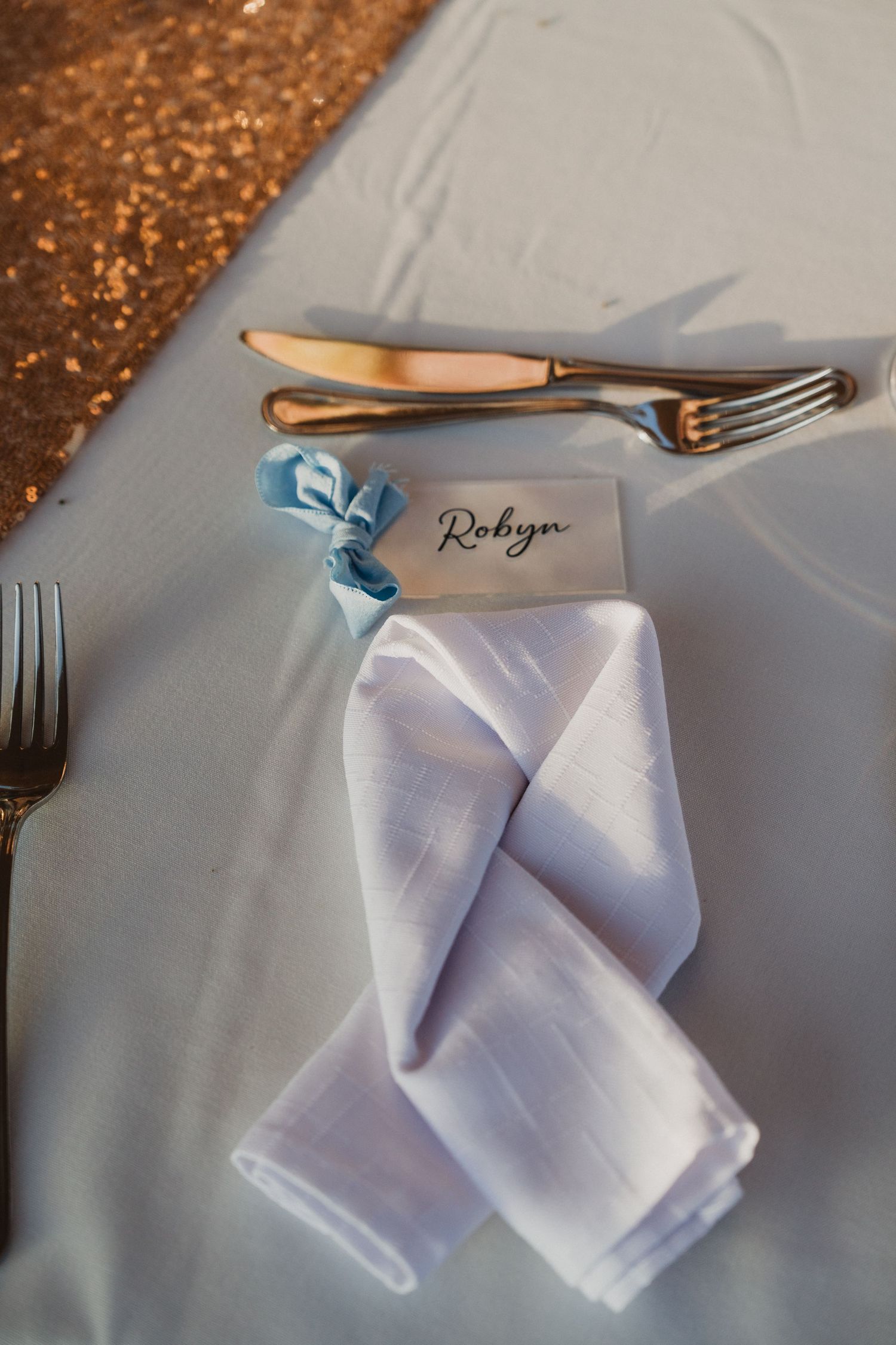 Place setting with white napkin and silverware on sequined table runner.