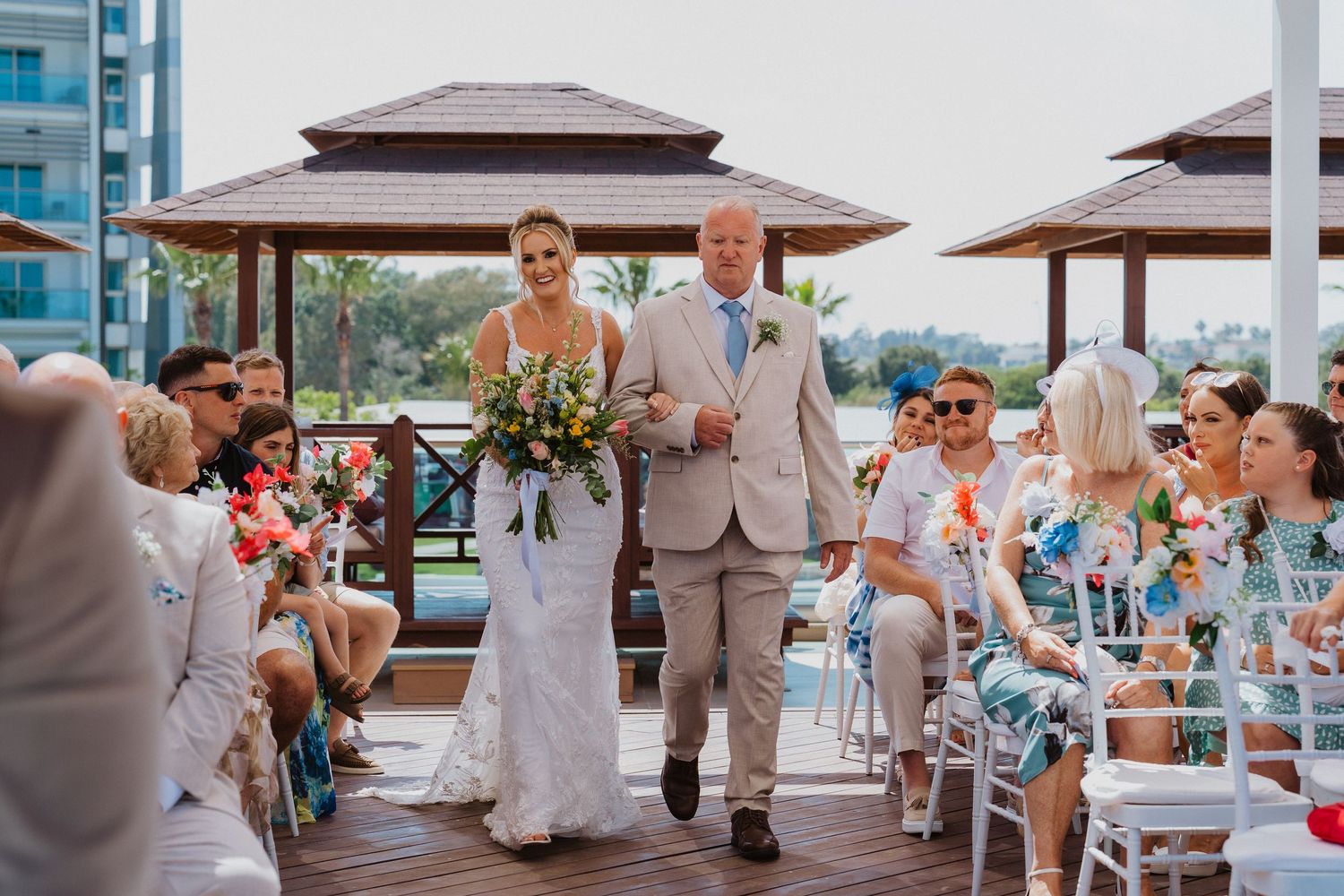 A wedding party celebrates at a beachside resort venue with palm trees and ocean views in the background.
