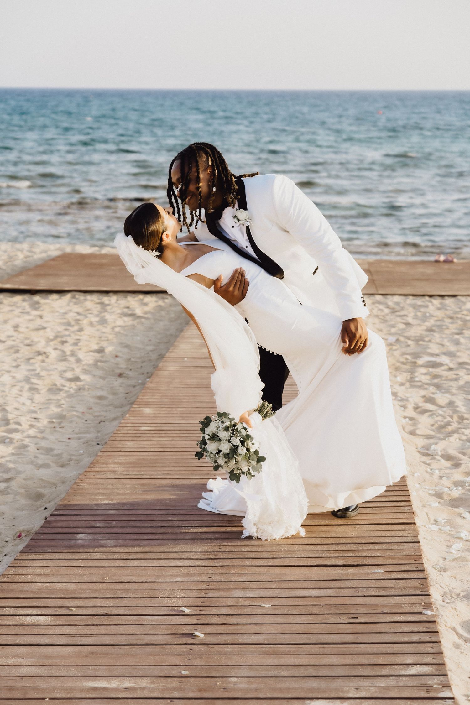 Romantic moment captured on wooden boardwalk by the ocean during sunset wedding.