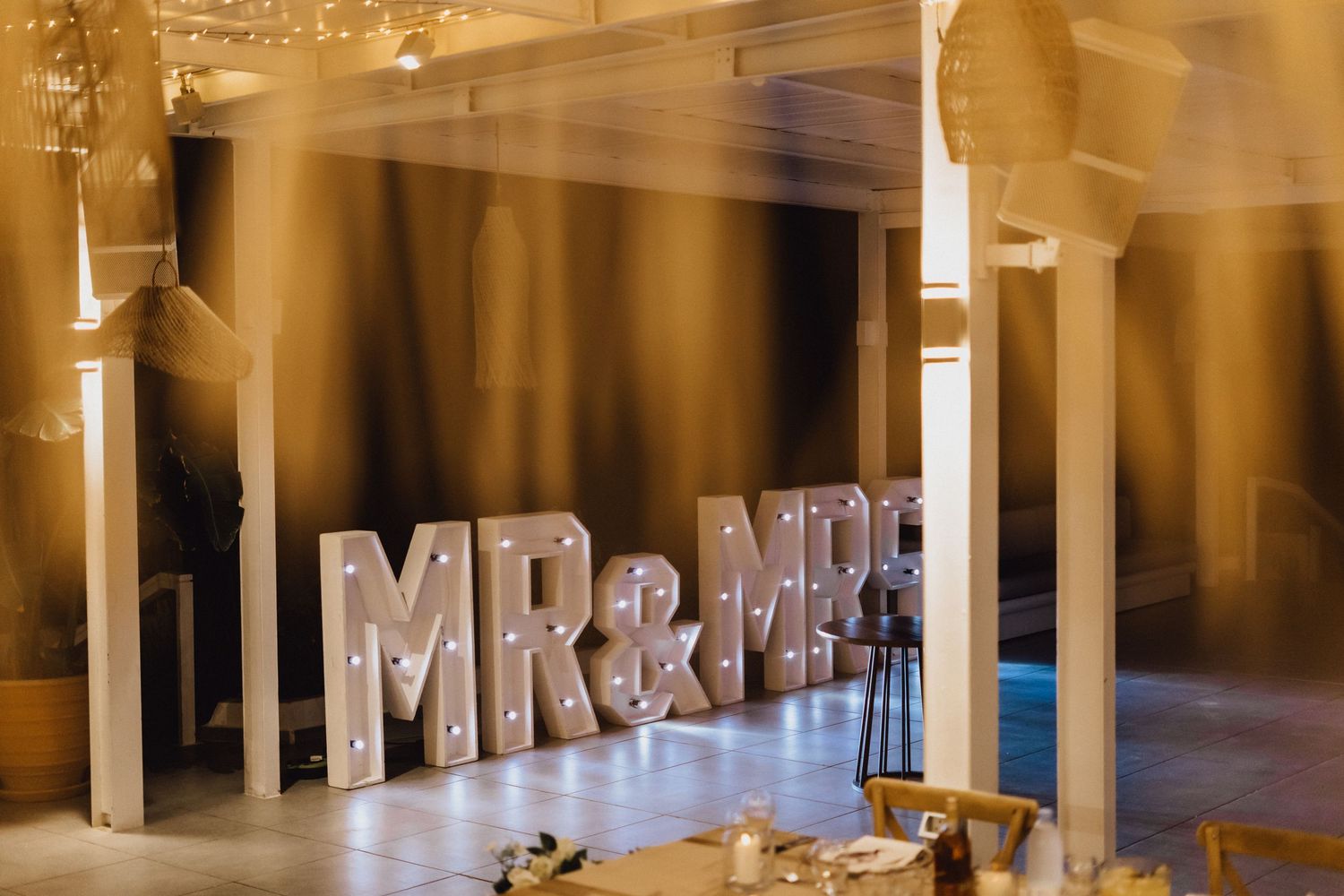Illuminated MR&MRS marquee letters displayed at wedding venue with columns and soft lighting.