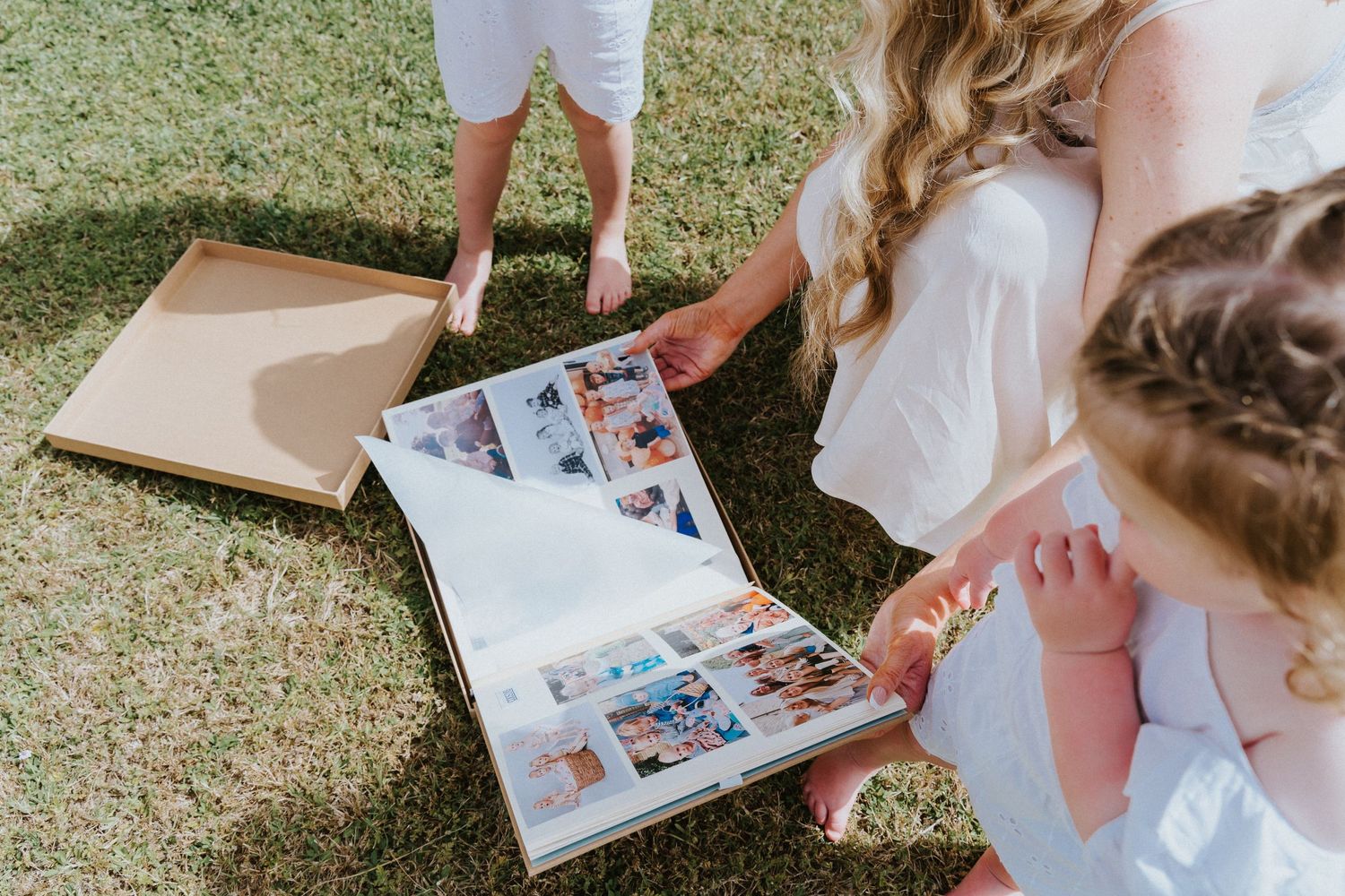 People looking through a photo album together on grass during a special occasion.