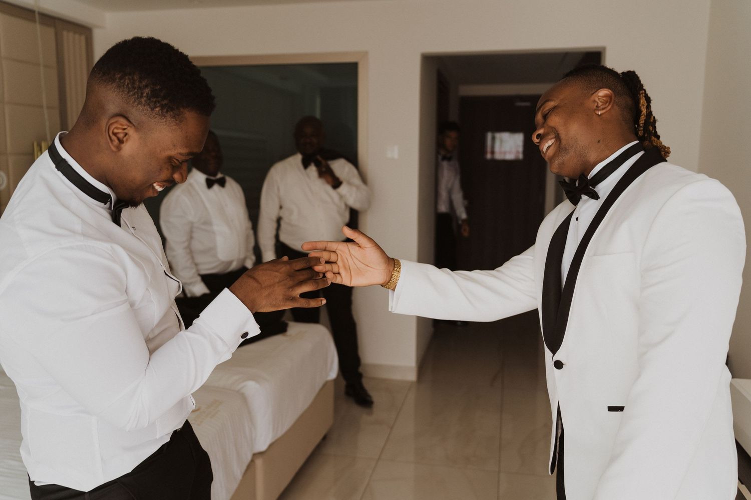 Two people in white tuxedo jackets share a joyful moment in a hotel hallway.