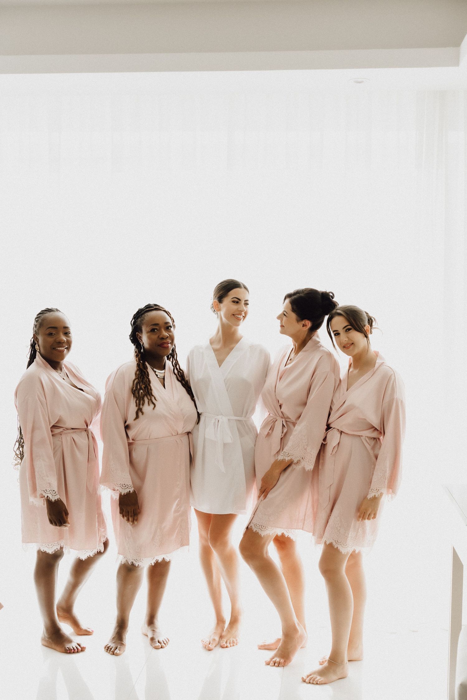 A group of women wearing matching pink and white robes stand together in a bright room.
